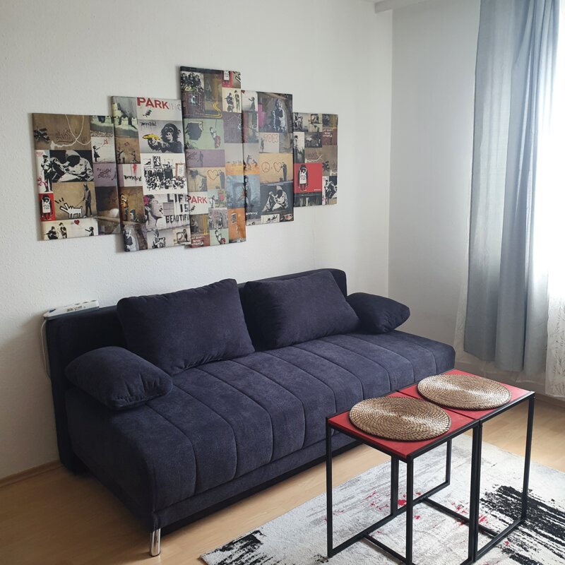 Stilvolles Wohnzimmer mit Banksy-Kunst & blauem Sofa – 2-Zimmer Wohnung, Kurzzeitmiete & Wohnen auf Zeit für 1 bis 6 Monate in Wels