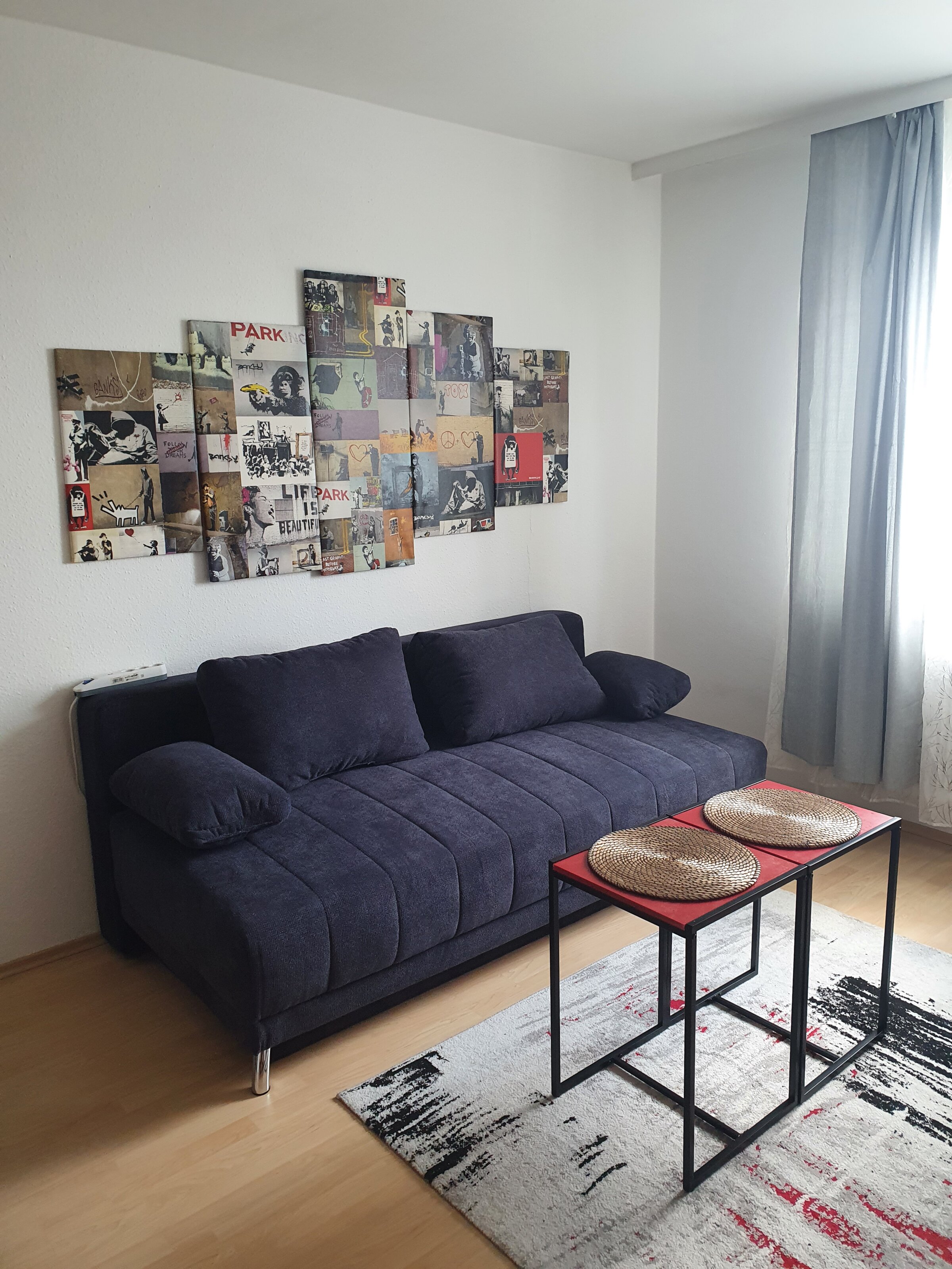 Stilvolles Wohnzimmer mit Banksy-Kunst & blauem Sofa – 2-Zimmer Wohnung, Kurzzeitmiete & Wohnen auf Zeit für 1 bis 6 Monate in Wels