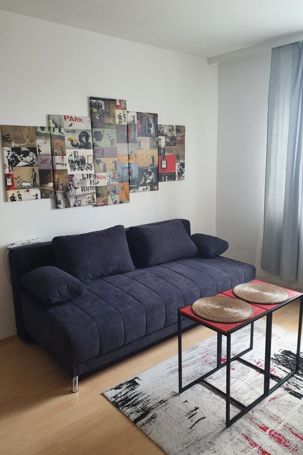Stilvolles Wohnzimmer mit Banksy-Kunst & blauem Sofa – 2-Zimmer Wohnung, Kurzzeitmiete & Wohnen auf Zeit für 1 bis 6 Monate in Wels
