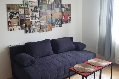 Stilvolles Wohnzimmer mit Banksy-Kunst & blauem Sofa – 2-Zimmer Wohnung, Kurzzeitmiete & Wohnen auf Zeit für 1 bis 6 Monate in Wels