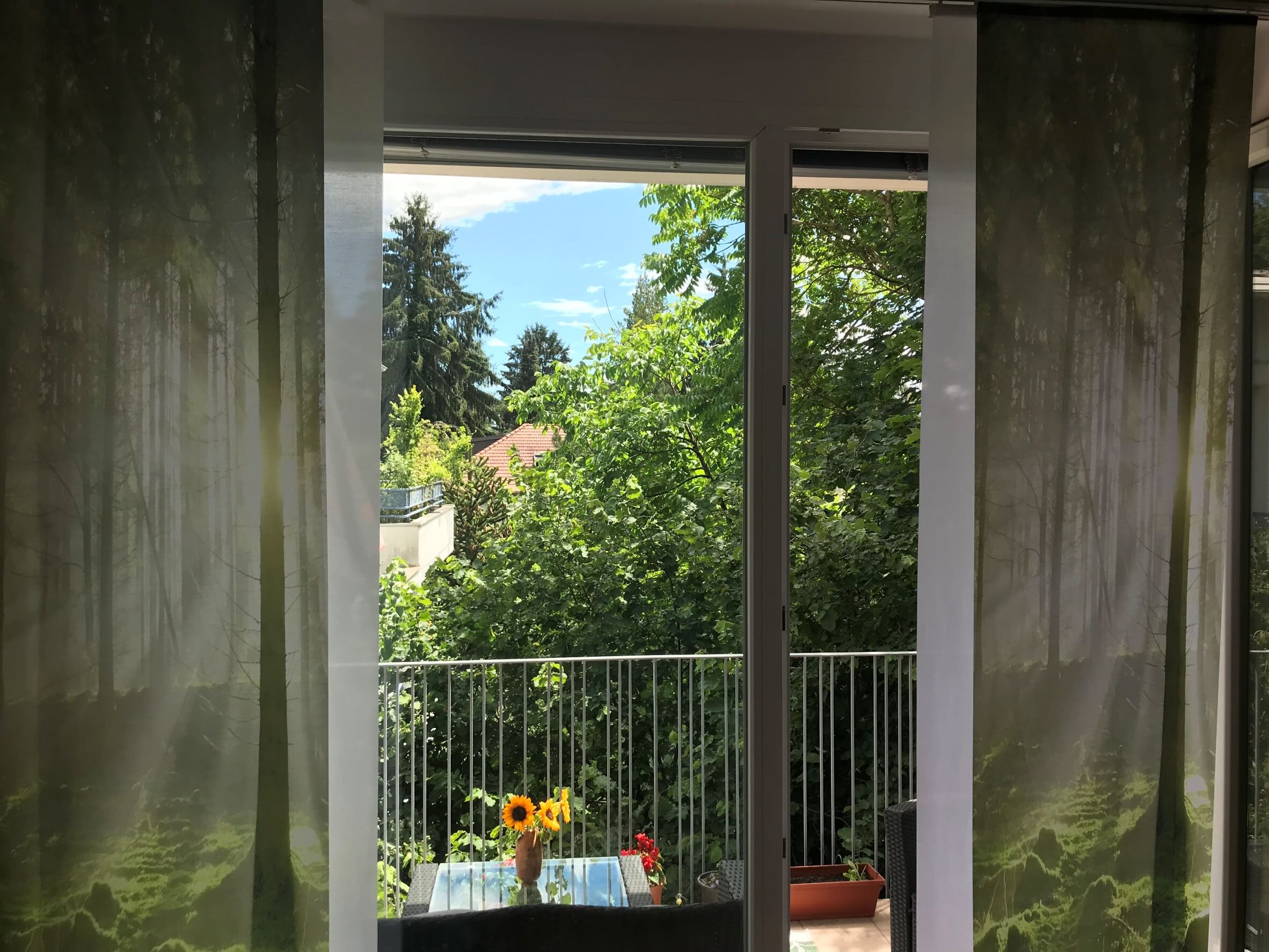 Blick vom Wohnbereich auf die extra große Terasse ins Grüne und auf umliegende Villen