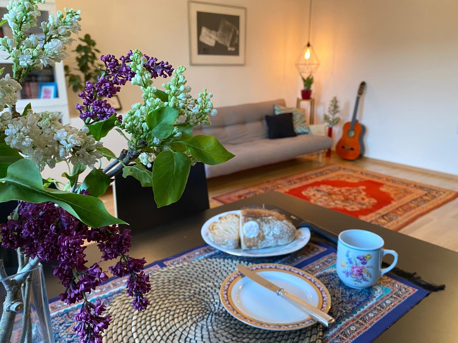 Wohnzimmer mit Flieder, Gitarre & gemütlichem Sofa – 2-Zimmer Wohnung, Kurzzeitmiete Wien, 1 bis 6 Monate