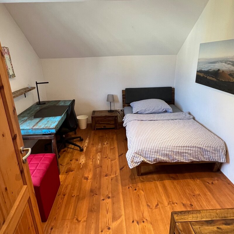 This inviting single room combines cosiness with functionality and is equipped with a comfortable single bed and a desk. It is the perfect retreat for guests looking for a quiet work area or a cozy reading spot. A small chest of drawers provides practical storage space for personal items. The well-thought-out furnishings create an atmosphere that invites both productivity and relaxation.
