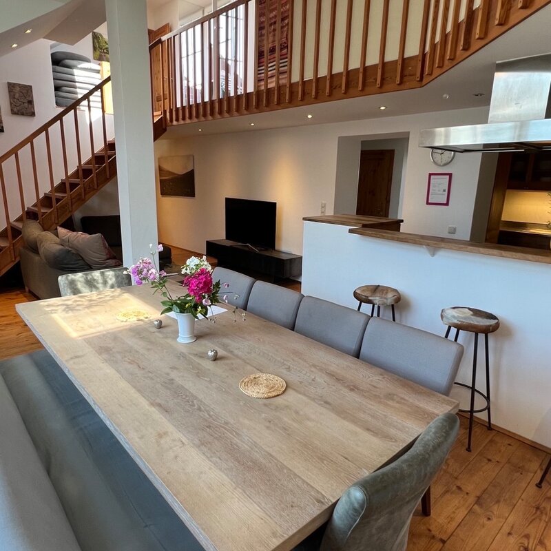 Unser großzügiges Wohn- und Esszimmer bildet das Herzstück der Wohnung, entworfen, um nahtlos Eleganz und Funktionalität zu vereinen. Die offene Raumgestaltung fördert ein geselliges Beisammensein, während die geschmackvolle Einrichtung und sanfte Beleuchtung eine warme, einladende Atmosphäre schaffen. Das Wohnzimmer, ausgestattet mit einer bequemen Sofalandschaft und einem Smart-TV, lädt zu gemütlichen Filmabenden ein. Der angrenzende Essbereich, mit einem modernen Tisch für 10 Personen, bietet den idealen Rahmen für gemeinsame Mahlzeiten. Große Fenster sorgen für reichlich Tageslicht, was diesen Raum perfekt für Entspannung und Unterhaltung macht.