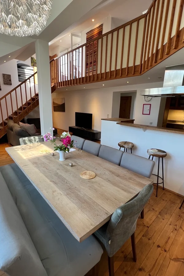 Unser großzügiges Wohn- und Esszimmer bildet das Herzstück der Wohnung, entworfen, um nahtlos Eleganz und Funktionalität zu vereinen. Die offene Raumgestaltung fördert ein geselliges Beisammensein, während die geschmackvolle Einrichtung und sanfte Beleuchtung eine warme, einladende Atmosphäre schaffen. Das Wohnzimmer, ausgestattet mit einer bequemen Sofalandschaft und einem Smart-TV, lädt zu gemütlichen Filmabenden ein. Der angrenzende Essbereich, mit einem modernen Tisch für 10 Personen, bietet den idealen Rahmen für gemeinsame Mahlzeiten. Große Fenster sorgen für reichlich Tageslicht, was diesen Raum perfekt für Entspannung und Unterhaltung macht.