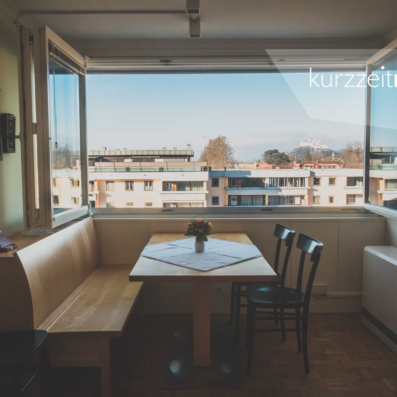 Dining area with large window & city view – 2-room apartment, short-term rental & temporary housing for 1 to 6 months in Aigen