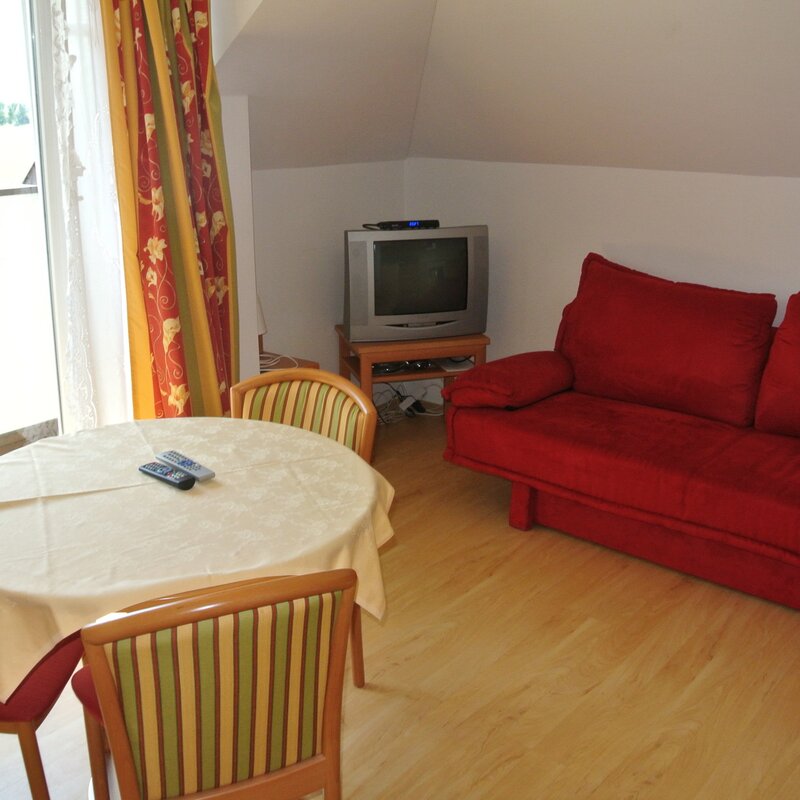 Helles Wohnzimmer mit rotem Sofa & Esstisch – 2-Zimmer-Wohnung zur Kurzzeitmiete & Wohnen auf Zeit für 1 bis 6 Monate in Anthering
