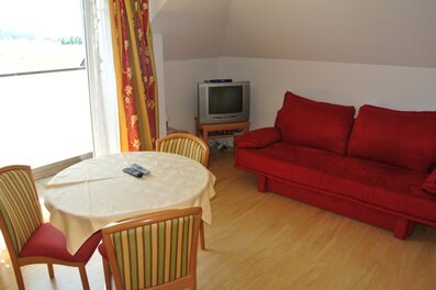 Helles Wohnzimmer mit rotem Sofa & Esstisch – 2-Zimmer-Wohnung zur Kurzzeitmiete & Wohnen auf Zeit für 1 bis 6 Monate in Anthering