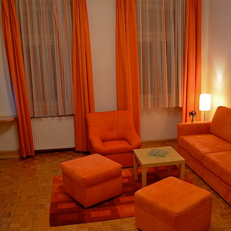 Wohnzimmer mit orangem Sofa & Sessel – 2-Zimmer Apartment, Kurzzeitmiete Wien, Wohnen auf Zeit 1 bis 6 Monate