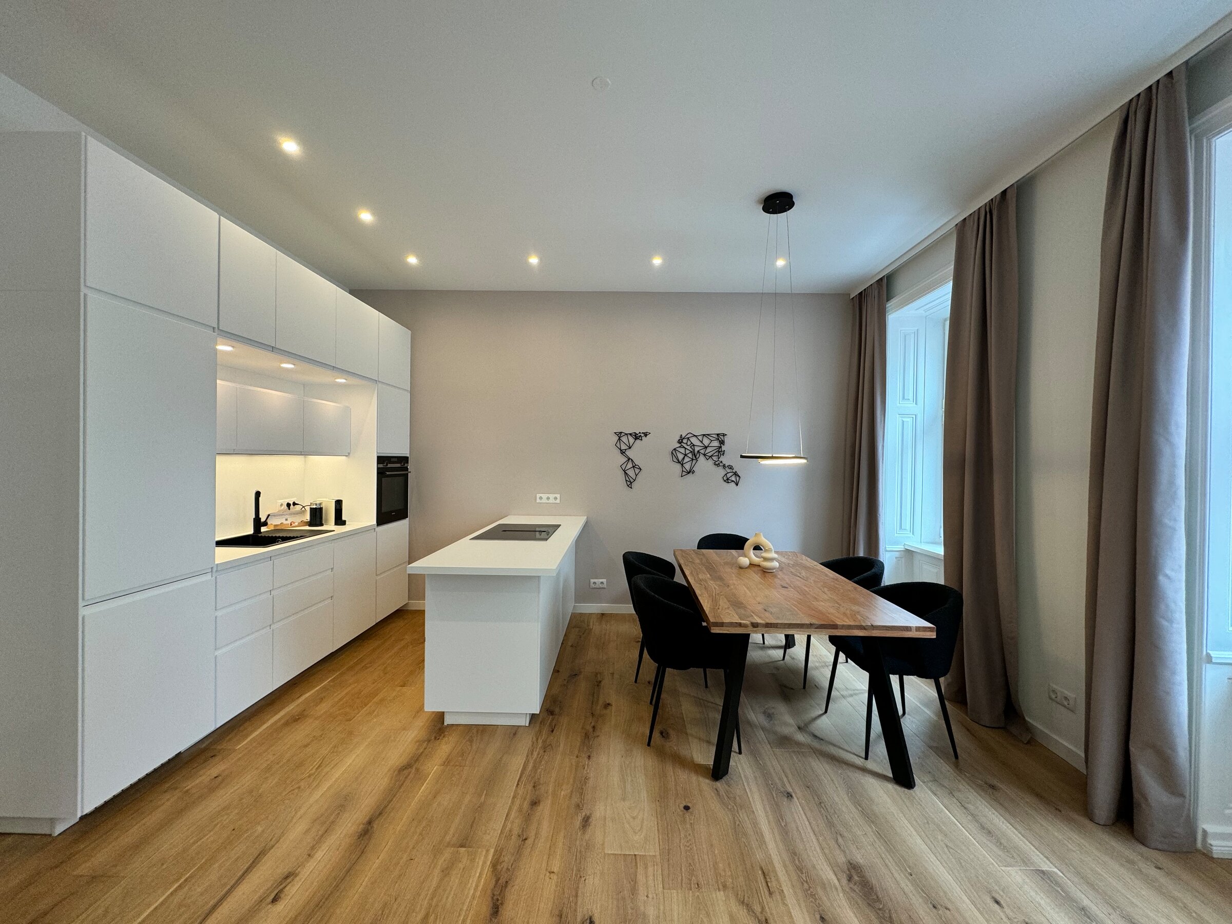 The open living and dining area features modern furnishings, a fully equipped kitchen, a large dining table, and stylish furniture. The large windows allow plenty of natural light, creating a bright and inviting atmosphere.