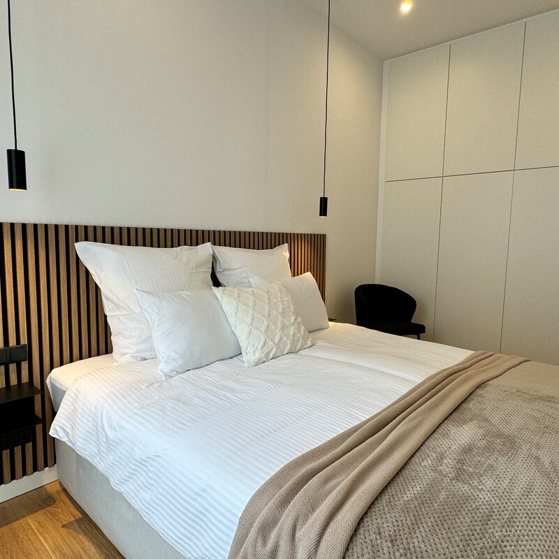 The stylish bedroom features a large, comfortable box spring bed, modern lighting, and a spacious built-in wardrobe. The built-in wardrobe provides ample space for your clothes and personal items, ensuring a neat and organized environment.