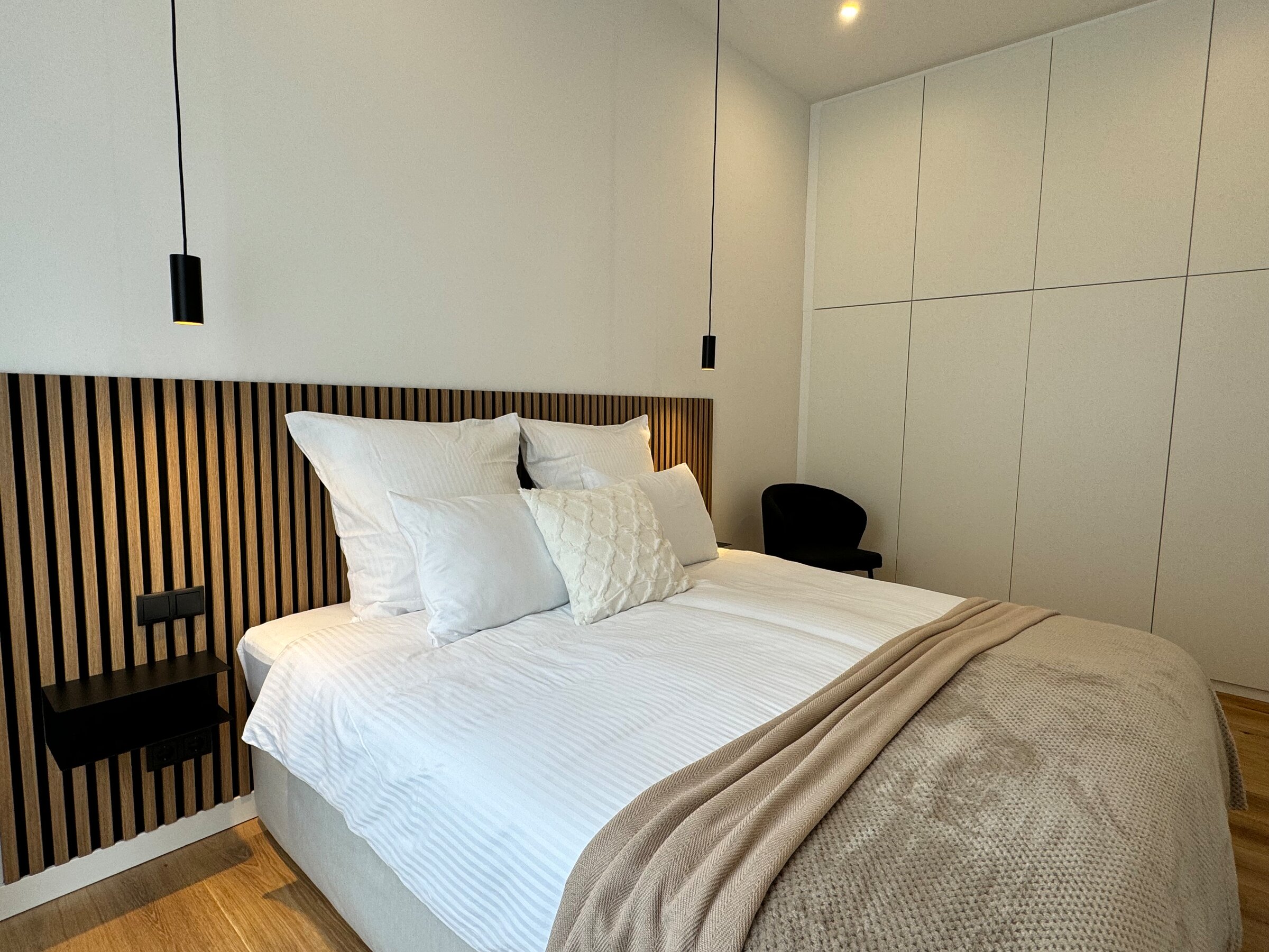 The stylish bedroom features a large, comfortable box spring bed, modern lighting, and a spacious built-in wardrobe. The built-in wardrobe provides ample space for your clothes and personal items, ensuring a neat and organized environment.