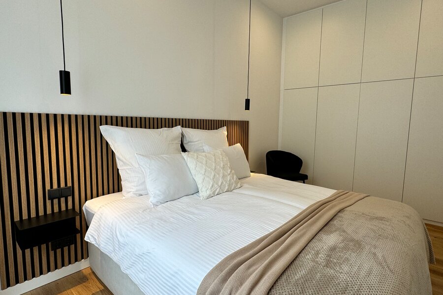 The stylish bedroom features a large, comfortable box spring bed, modern lighting, and a spacious built-in wardrobe. The built-in wardrobe provides ample space for your clothes and personal items, ensuring a neat and organized environment.