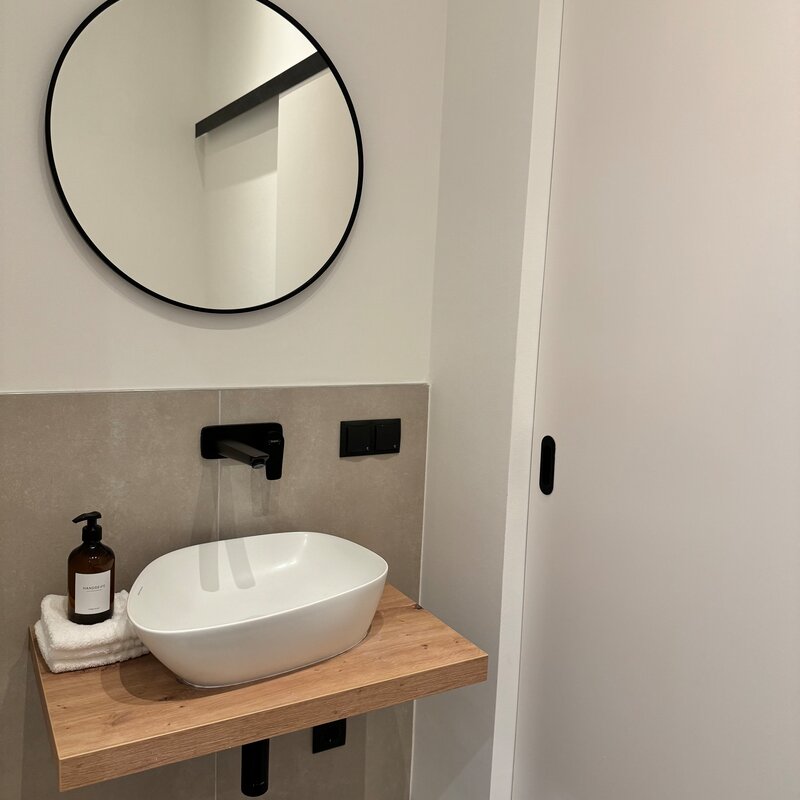 Das elegante Gäste-WC verfügt über ein modernes Waschbecken und eine praktische Schiebetür, die zusätzlichen Stauraum verbirgt. Das schlichte Design und die stilvollen Details machen es zu einem praktischen und ästhetischen Raum.