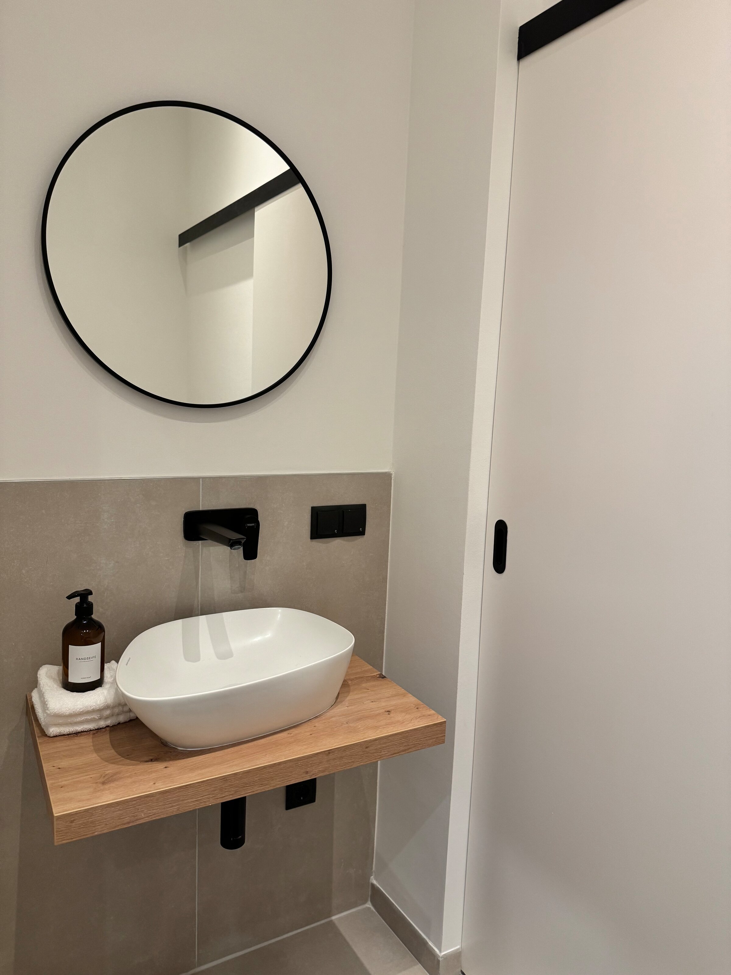 Das elegante Gäste-WC verfügt über ein modernes Waschbecken und eine praktische Schiebetür, die zusätzlichen Stauraum verbirgt. Das schlichte Design und die stilvollen Details machen es zu einem praktischen und ästhetischen Raum.