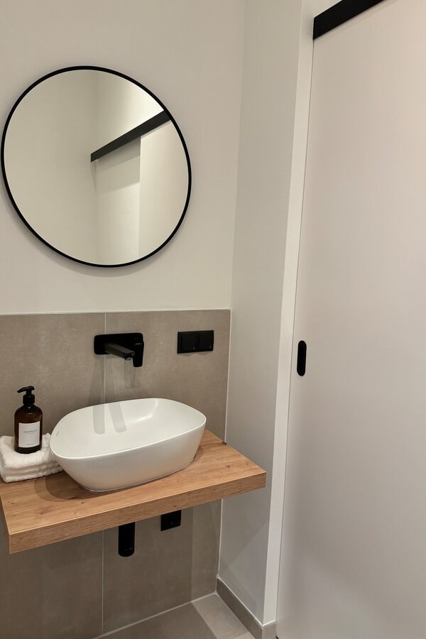 Das elegante Gäste-WC verfügt über ein modernes Waschbecken und eine praktische Schiebetür, die zusätzlichen Stauraum verbirgt. Das schlichte Design und die stilvollen Details machen es zu einem praktischen und ästhetischen Raum.