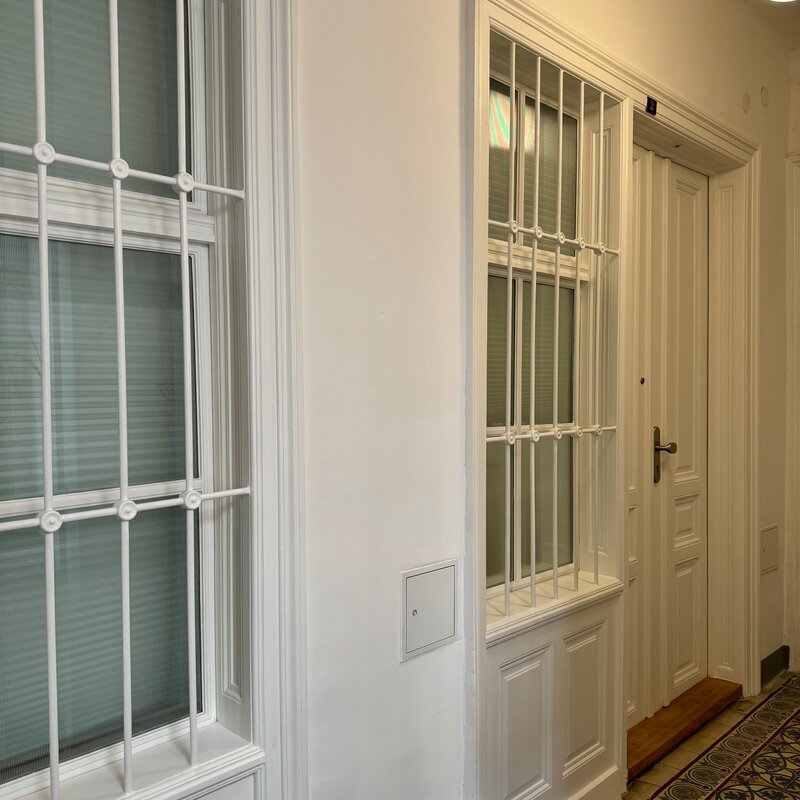 Der Eingang zur Wohnung von außen. Das Fenster aus geriffeltem Glas zum Hausflur lässt natürliches Licht herein und kann mit einem Rollo verdunkelt werden, um Privatsphäre zu gewährleisten. Der zusätzliche Sichtschutz sorgt für eine angenehme und geschützte Wohnatmosphäre.