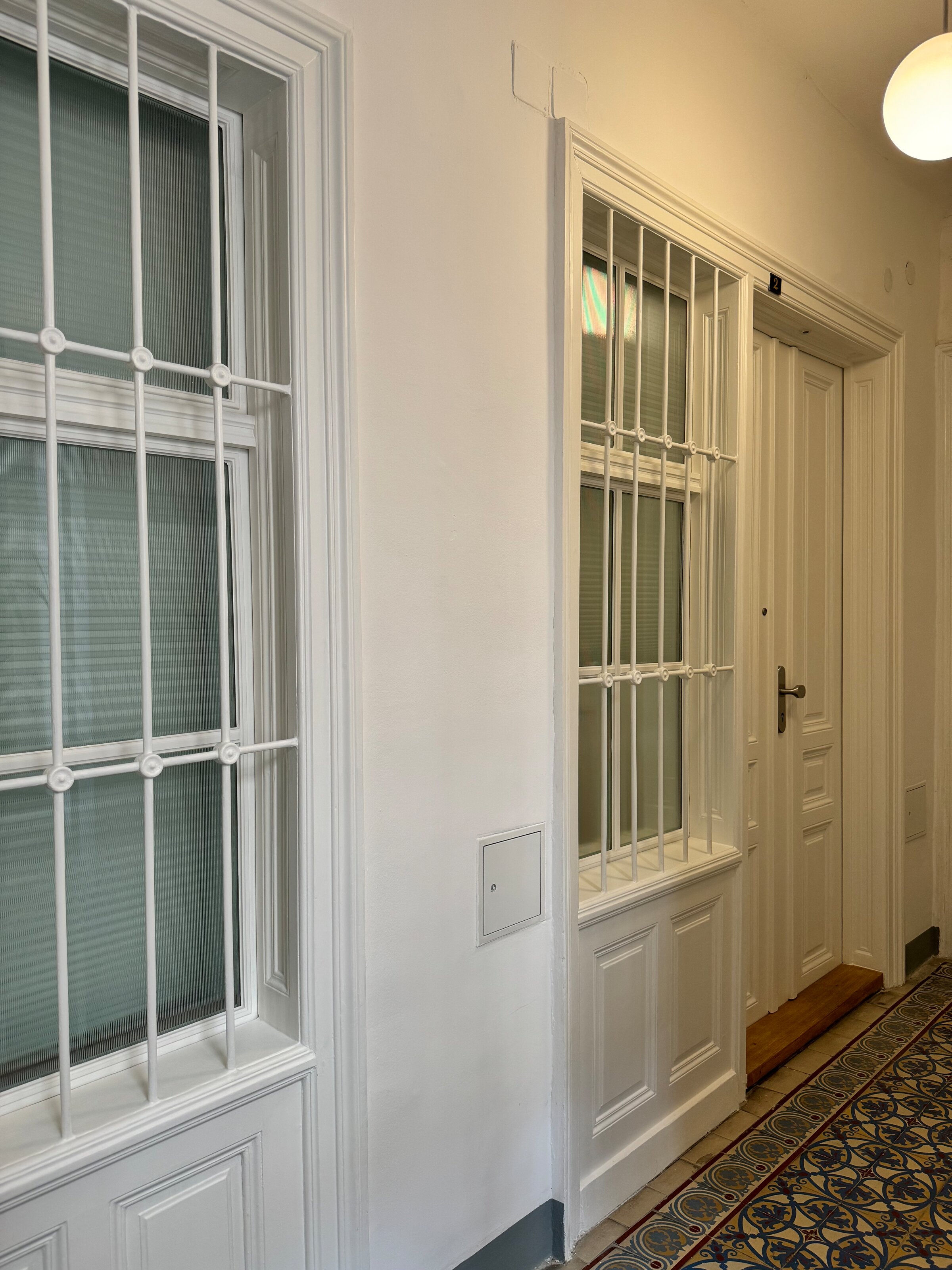 Der Eingang zur Wohnung von außen. Das Fenster aus geriffeltem Glas zum Hausflur lässt natürliches Licht herein und kann mit einem Rollo verdunkelt werden, um Privatsphäre zu gewährleisten. Der zusätzliche Sichtschutz sorgt für eine angenehme und geschützte Wohnatmosphäre.