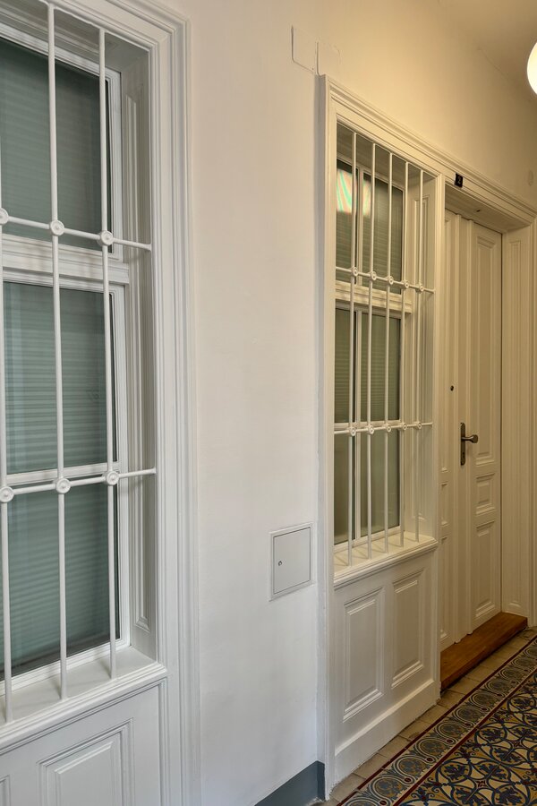 Der Eingang zur Wohnung von außen. Das Fenster aus geriffeltem Glas zum Hausflur lässt natürliches Licht herein und kann mit einem Rollo verdunkelt werden, um Privatsphäre zu gewährleisten. Der zusätzliche Sichtschutz sorgt für eine angenehme und geschützte Wohnatmosphäre.