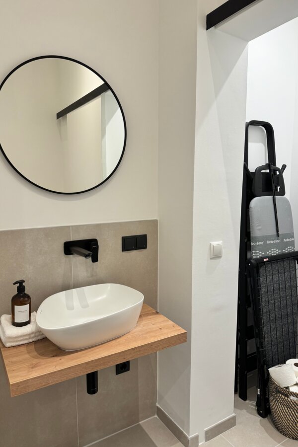 Die elegante Gästetoilette verfügt über ein modernes Waschbecken und eine geöffnete Schiebetür, die den zusätzlichen Stauraum zeigt.