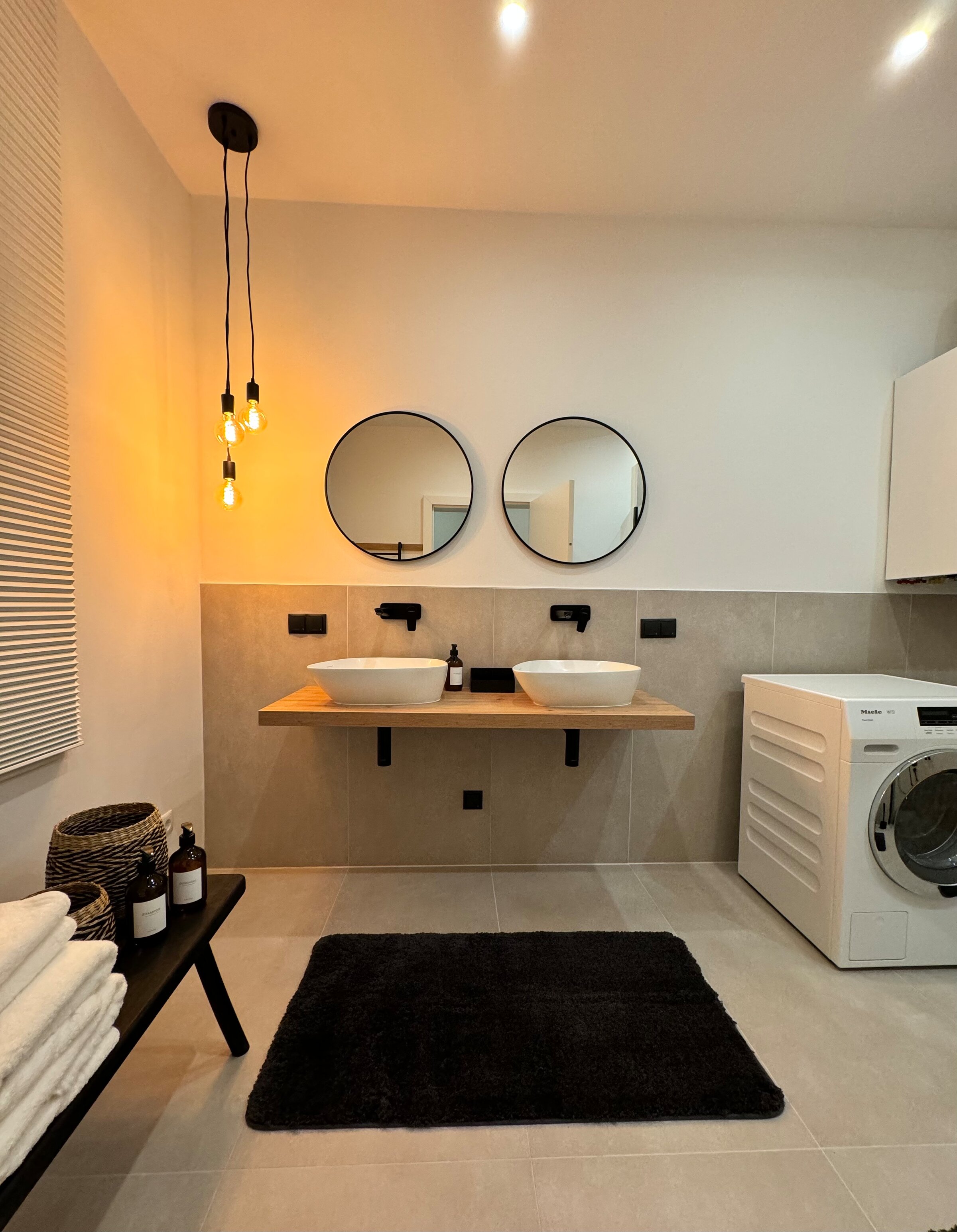 The bathroom is modern and stylishly furnished, featuring two sinks, a spacious shower, and a toilet. A washing machine adds extra convenience. The tasteful lighting and elegant details create a relaxing atmosphere.