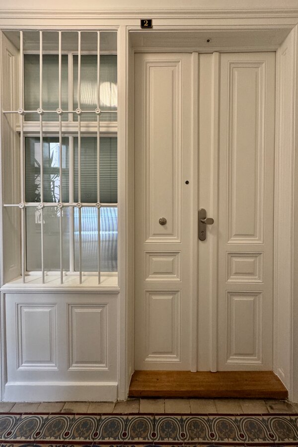 Die Eingangstür der Wohnung von außen. Das Fenster aus geriffeltem Glas zum Hausflur lässt Licht in die Wohnung und kann mit einem Rollo verdunkelt werden. Es sorgt zusätzlich für ausreichenden Sichtschutz und gewährleistet Privatsphäre.