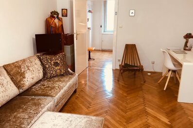 Helles Wohnzimmer mit Fischgrätparkett, Samtsofa & Arbeitsplatz – 2-Zimmer Wohnung zur Kurzzeitmiete Wien