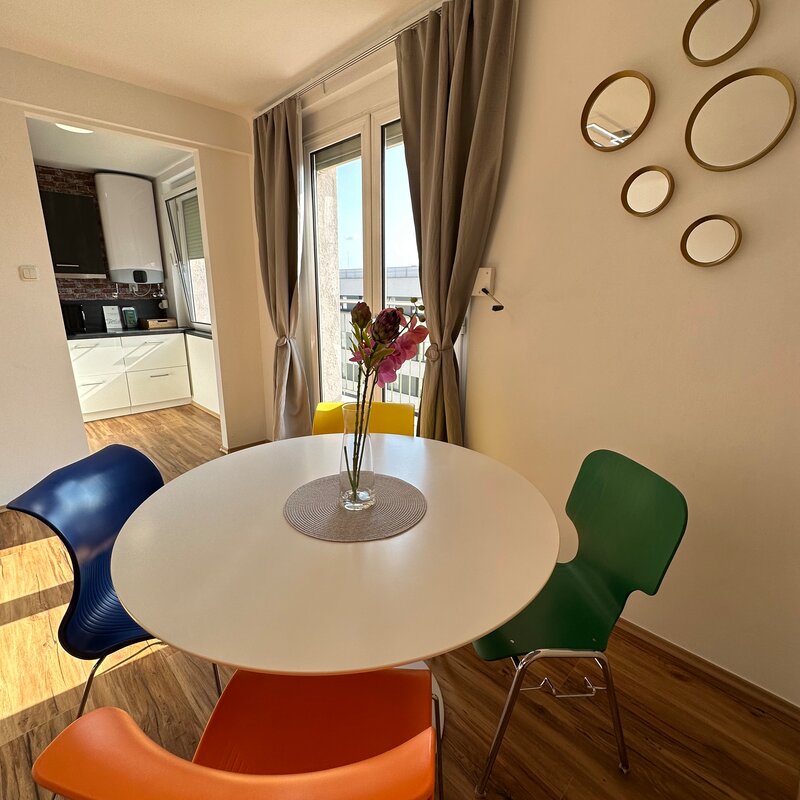 Dining area with colorful chairs & balcony – 3-room apartment, short-term rental & temporary housing for 1 to 6 months in Graz