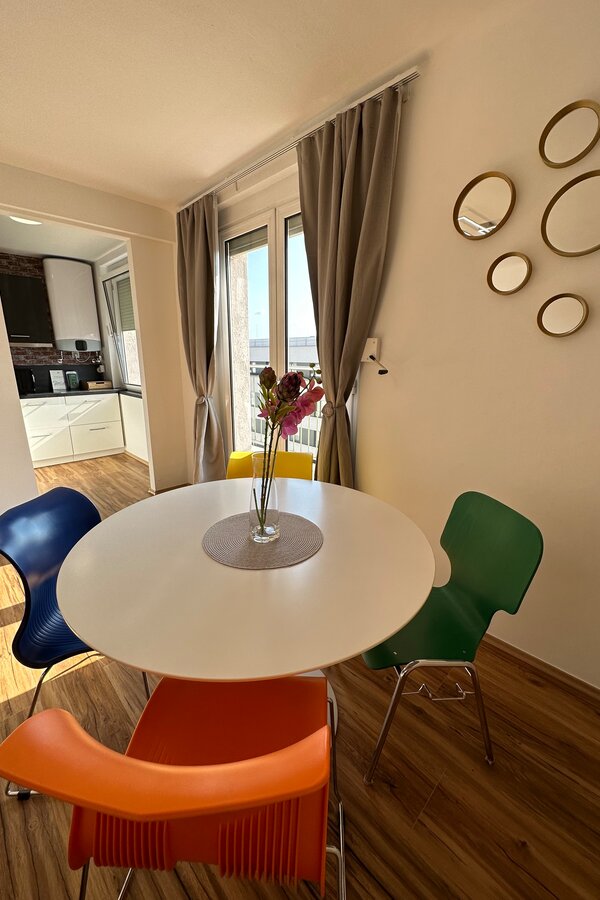 Dining area with colorful chairs & balcony – 3-room apartment, short-term rental & temporary housing for 1 to 6 months in Graz