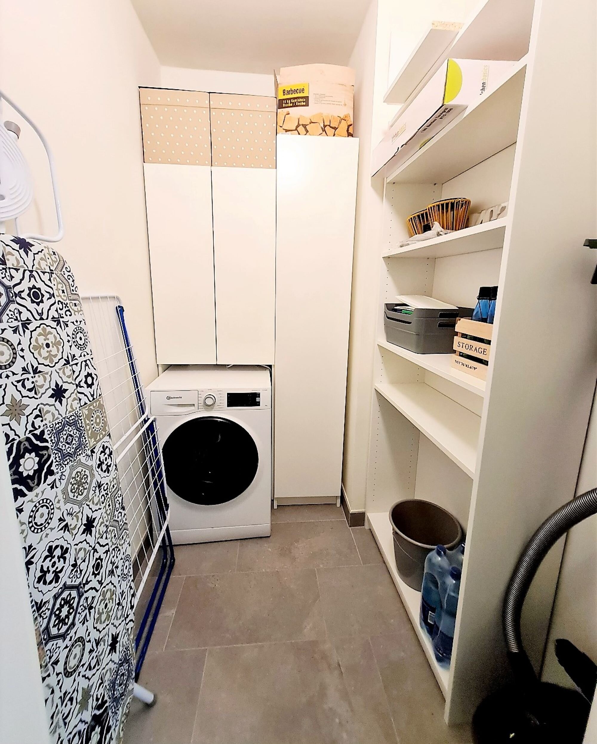Abstellraum mit Waschmaschine, Dampfbügestation, Bügelbrett, Wäscheständer, Staubsauger und diversen Reinigungsutensilien