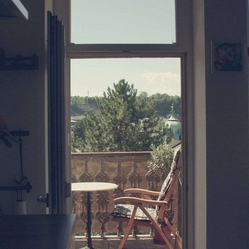 Balcony with wooden chair & city view: 2-room apartment for short-term rental & temporary housing for 1 to 6 months in Salzburg