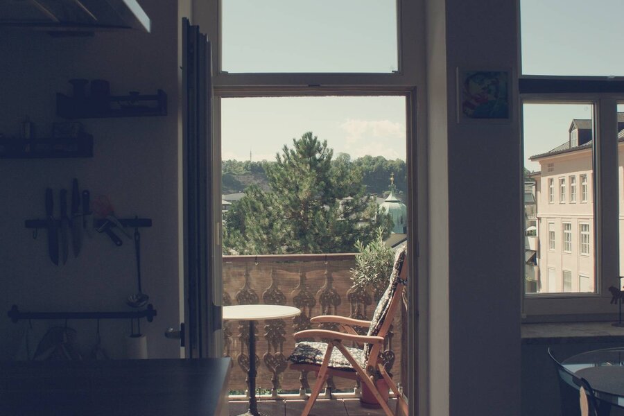Balcony with wooden chair & city view: 2-room apartment for short-term rental & temporary housing for 1 to 6 months in Salzburg