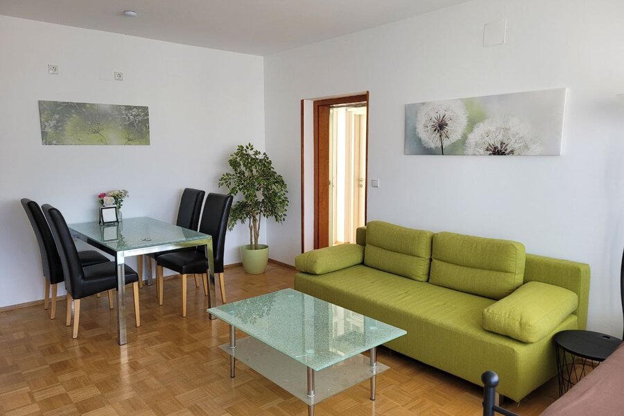 Bright living & dining area, glass table & green sofa – 3-room apartment, short-term rental Graz, temporary housing 1 to 6 months