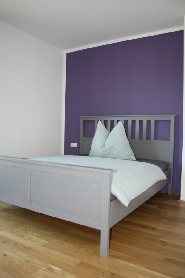 Helles Schlafzimmer mit grauem Holzbett & lila Akzentwand – 4-Zimmer-Wohnung, Kurzzeitmiete Innsbruck, Wohnen auf Zeit 1–6 Monate