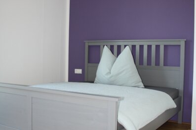 Helles Schlafzimmer mit grauem Holzbett & lila Akzentwand – 4-Zimmer-Wohnung, Kurzzeitmiete Innsbruck, Wohnen auf Zeit 1–6 Monate