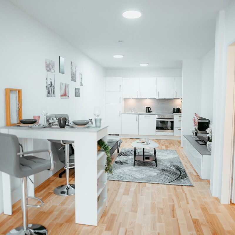 Wohnzimmer mit bequeme ausziehbarem Sofa, Couchtisch, elegantem Teppich, Flachbildfernseher und Bartisch, außerdem ist die voll ausgestattete Küche sichtbar. Direkter Blick auf die Terrasse. | © All rights reserved