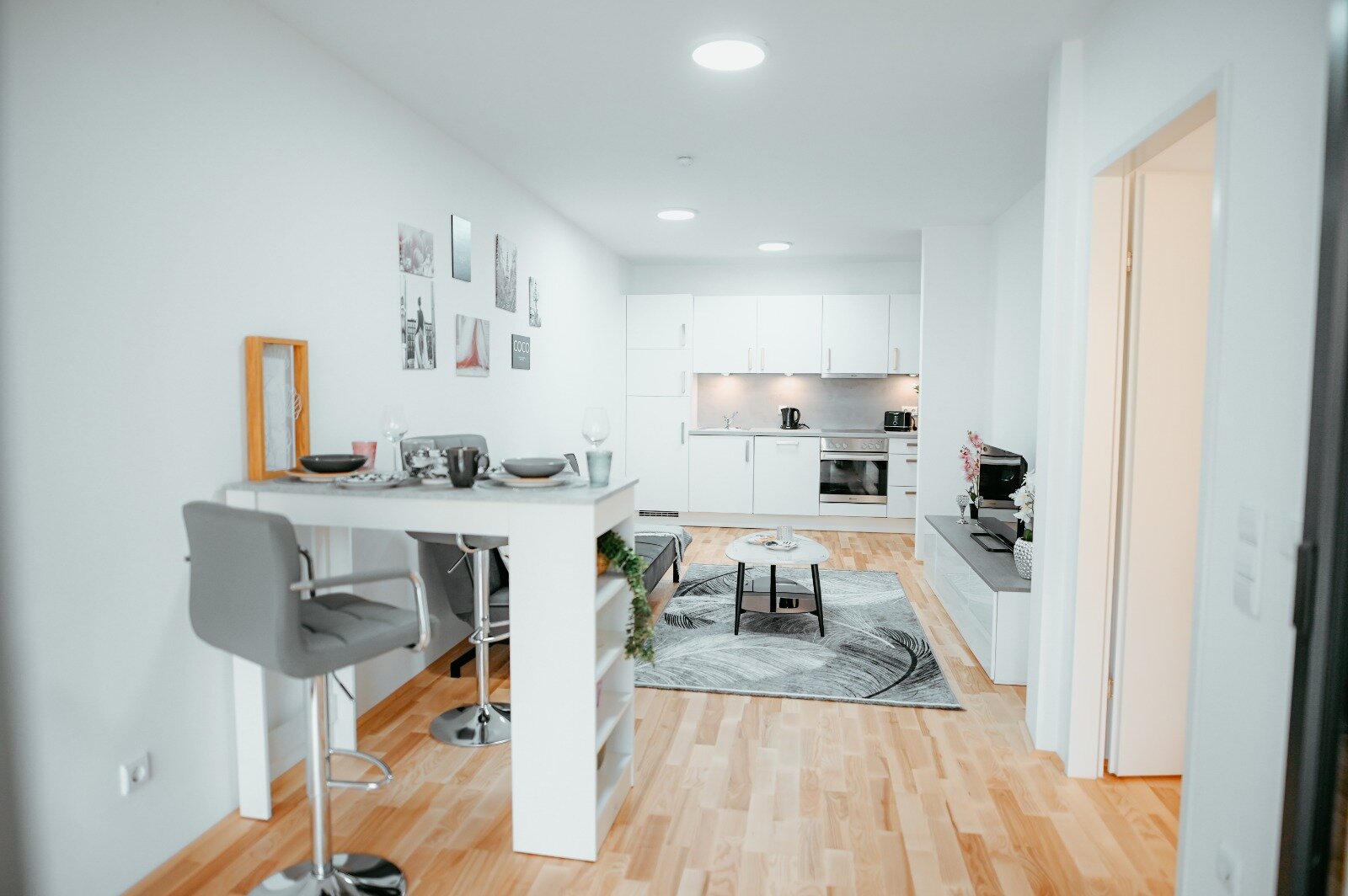 Wohnzimmer mit bequeme ausziehbarem Sofa, Couchtisch, elegantem Teppich, Flachbildfernseher und Bartisch, außerdem ist die voll ausgestattete Küche sichtbar. Direkter Blick auf die Terrasse. | © All rights reserved