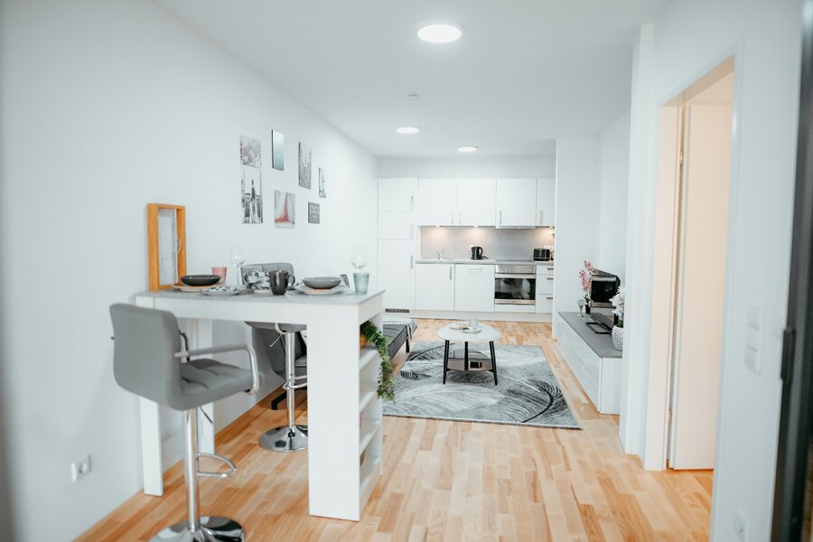 Wohnzimmer mit bequeme ausziehbarem Sofa, Couchtisch, elegantem Teppich, Flachbildfernseher und Bartisch, außerdem ist die voll ausgestattete Küche sichtbar. Direkter Blick auf die Terrasse. | © All rights reserved