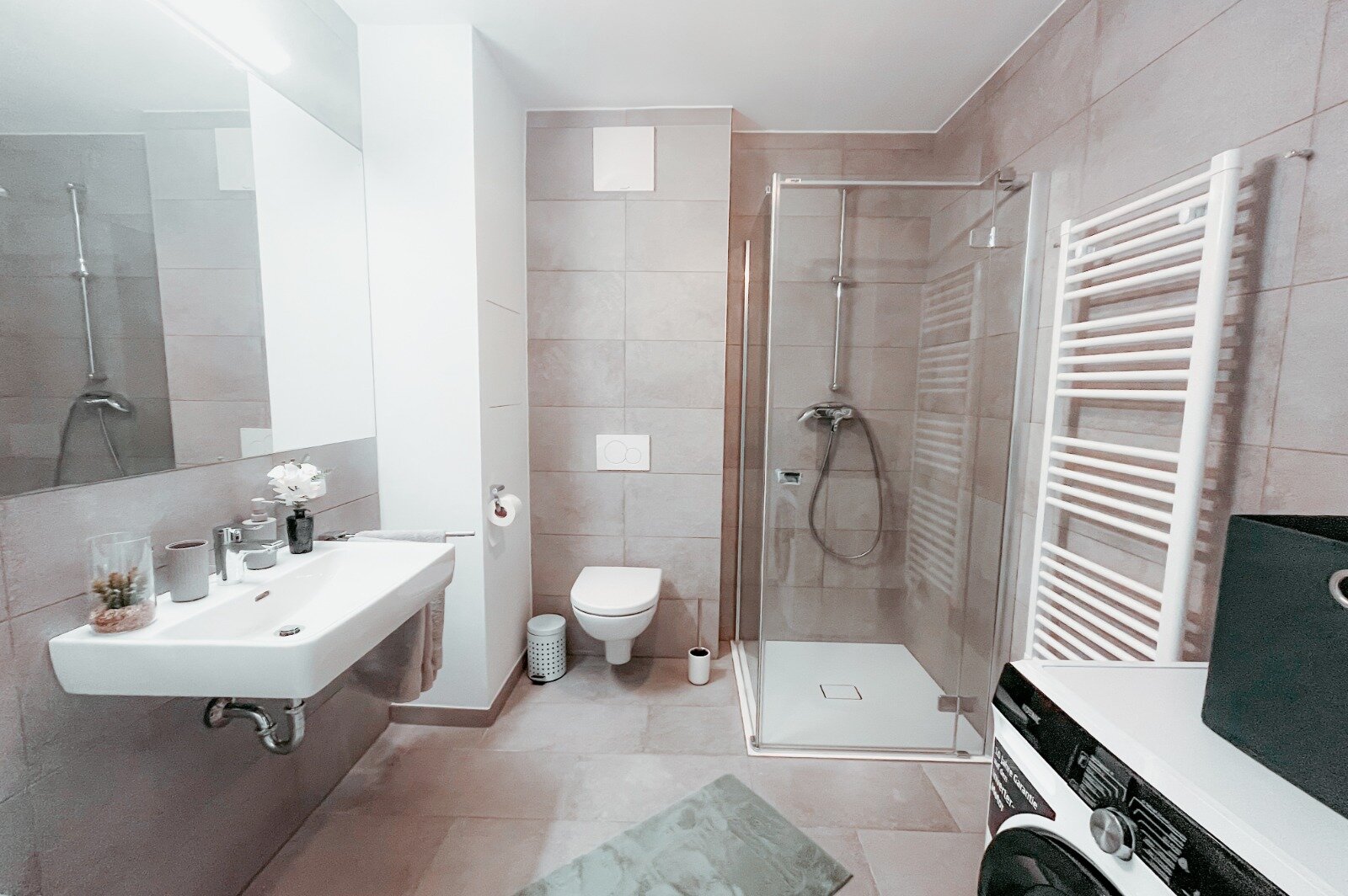 Badezimmer mit großem Spiegel, Waschbecken, Duschkabine, Waschmaschine mit Wasch- und Trockenfunktion, eingerichtet im eleganten Stil. | © All rights reserved