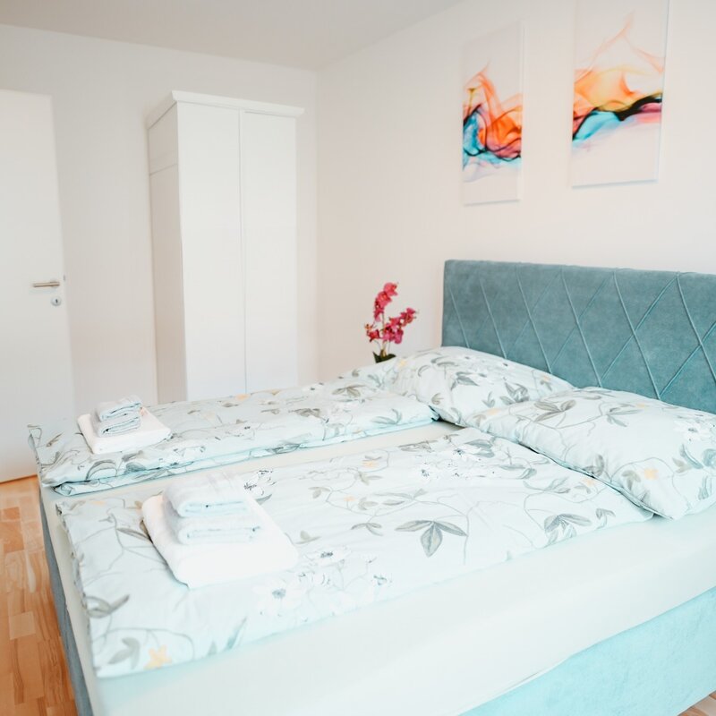 Schlafzimmer mit großem Doppelbett, in einer entspannenden Atmosphäre in Mintgrün, mit ausgewählten Dekorationsdetails, Kleiderschrank und zwei Nachttischen mit Lampe. | © All rights reserved