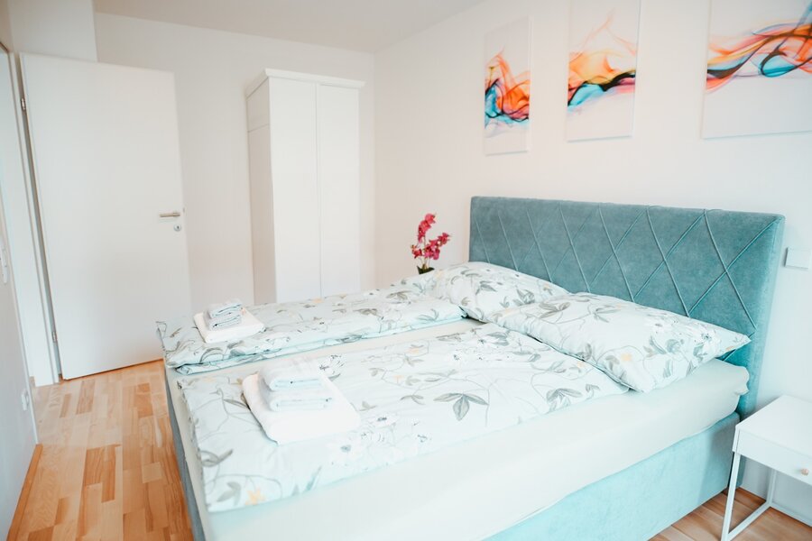 Schlafzimmer mit großem Doppelbett, in einer entspannenden Atmosphäre in Mintgrün, mit ausgewählten Dekorationsdetails, Kleiderschrank und zwei Nachttischen mit Lampe. | © All rights reserved