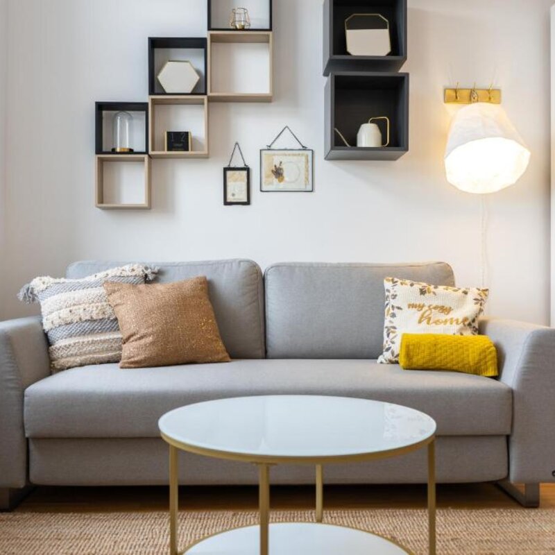 Bright living room with grey sofa & wall shelves – 1-room apartment, short-term rental, temporary housing 1 to 6 months, Vienna