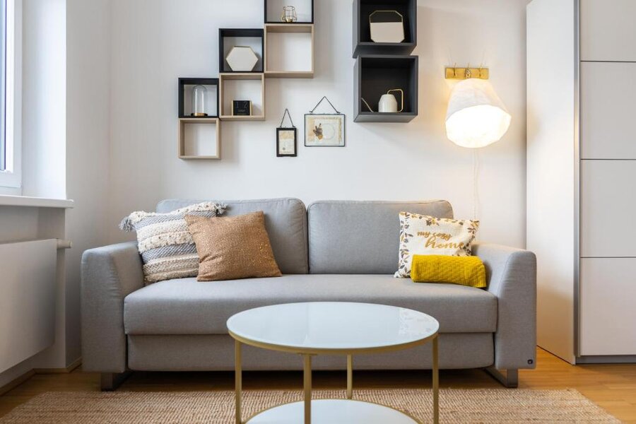 Bright living room with grey sofa & wall shelves – 1-room apartment, short-term rental, temporary housing 1 to 6 months, Vienna