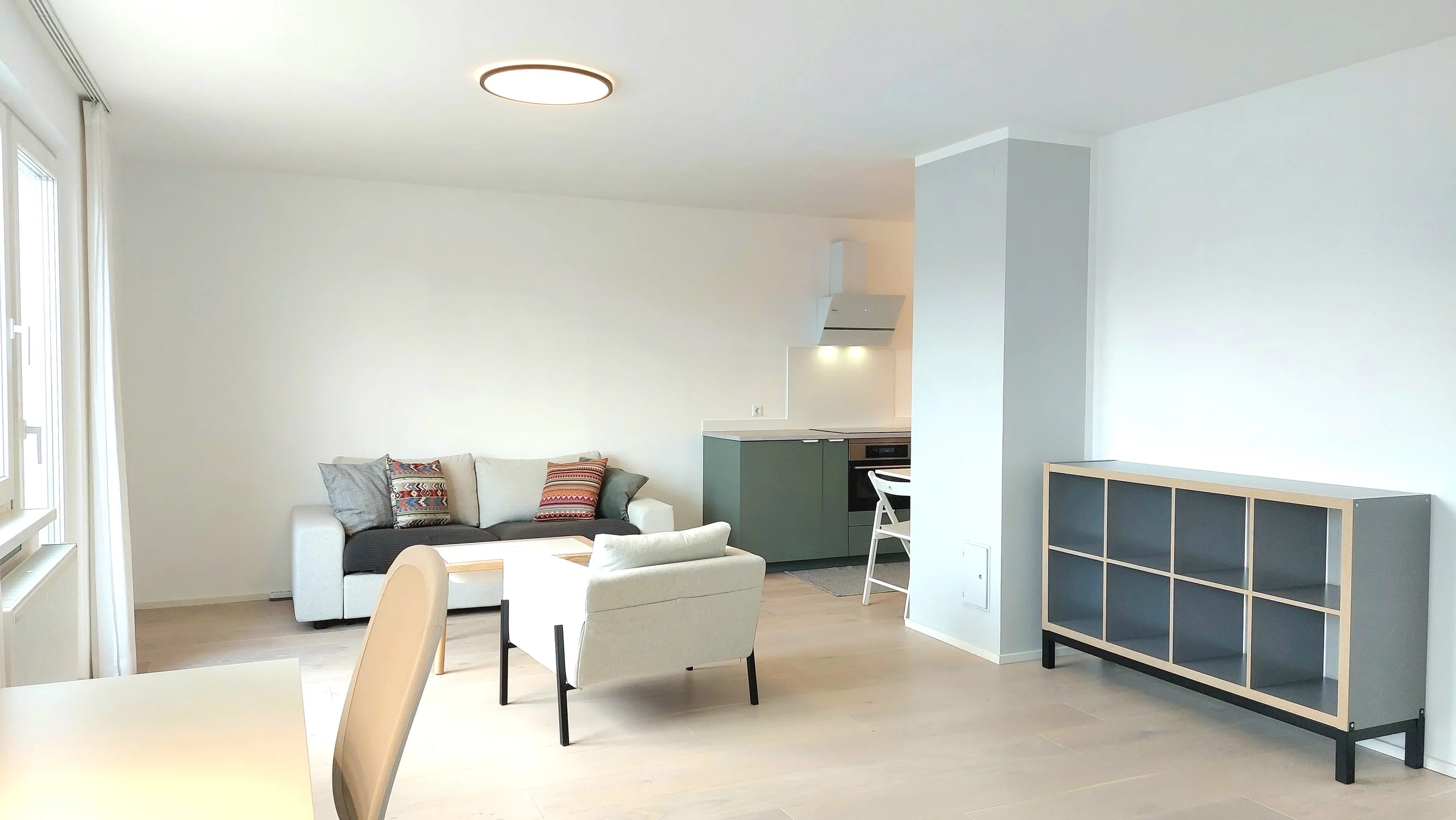 Wohnzimmer mit Arbreitsplatz und angeschlossener Küche