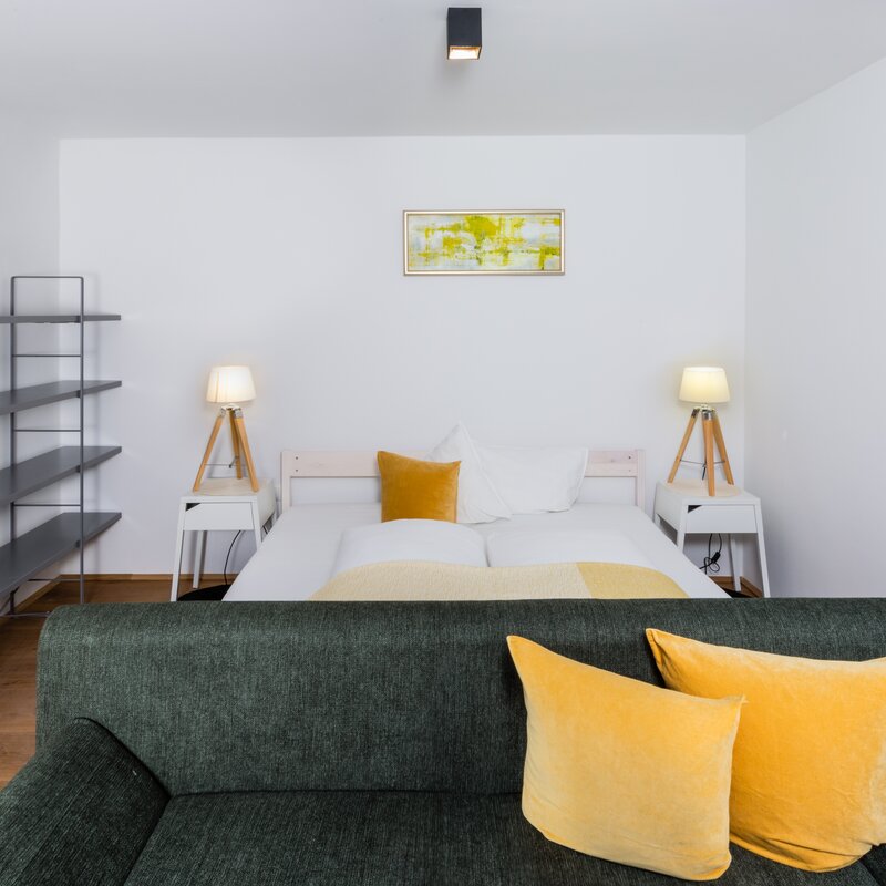 Helles Wohnschlafzimmer mit grünem Sofa & Doppelbett – 2-Zimmer Wohnung zur Kurzzeitmiete & Wohnen auf Zeit für 1 bis 6 Monate in Innsbruck