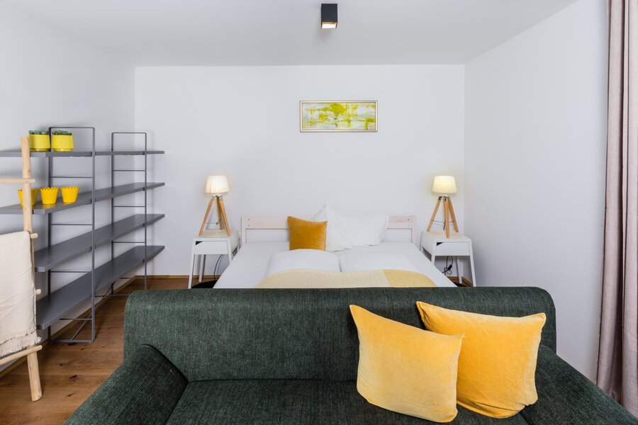 Helles Wohnschlafzimmer mit grünem Sofa & Doppelbett – 2-Zimmer Wohnung zur Kurzzeitmiete & Wohnen auf Zeit für 1 bis 6 Monate in Innsbruck