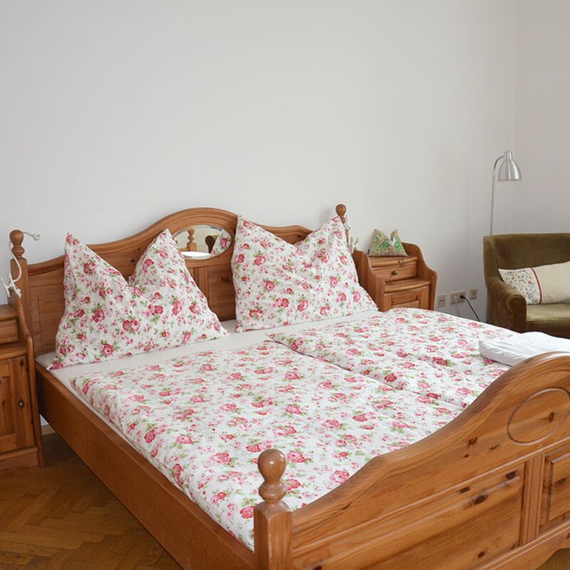 Cozy bedroom with wooden bed & floral bedding – 1-room apartment for short-term rental in Vienna