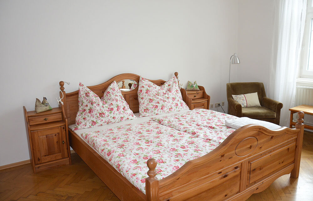 Cozy bedroom with wooden bed & floral bedding – 1-room apartment for short-term rental in Vienna