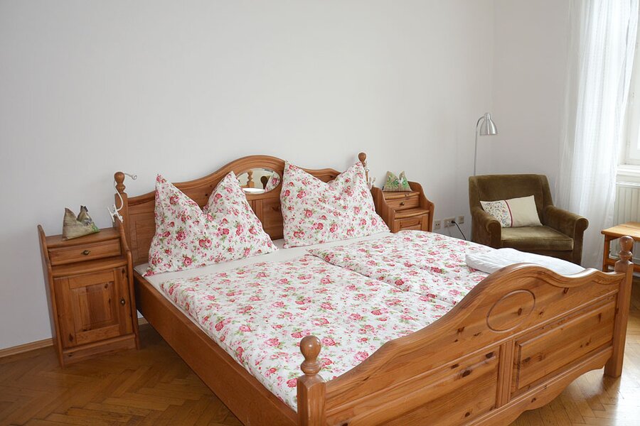 Cozy bedroom with wooden bed & floral bedding – 1-room apartment for short-term rental in Vienna