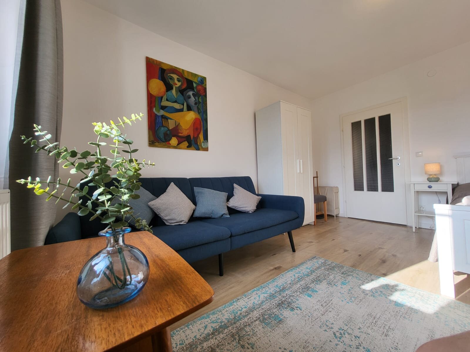 Helles Wohnzimmer mit blauem Sofa & Kunstwerk – 2-Zimmer Wohnung, Kurzzeitmiete & Wohnen auf Zeit für 1 bis 6 Monate in Melk